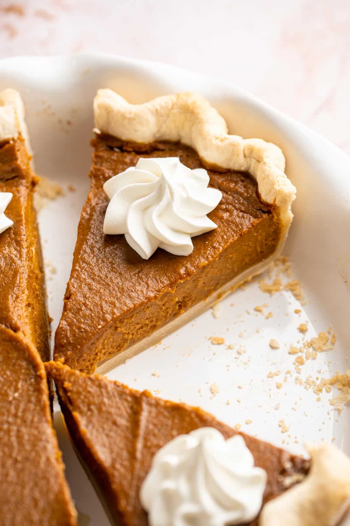 Slice of pumpkin pie in a pie plate topped with whipped cream.