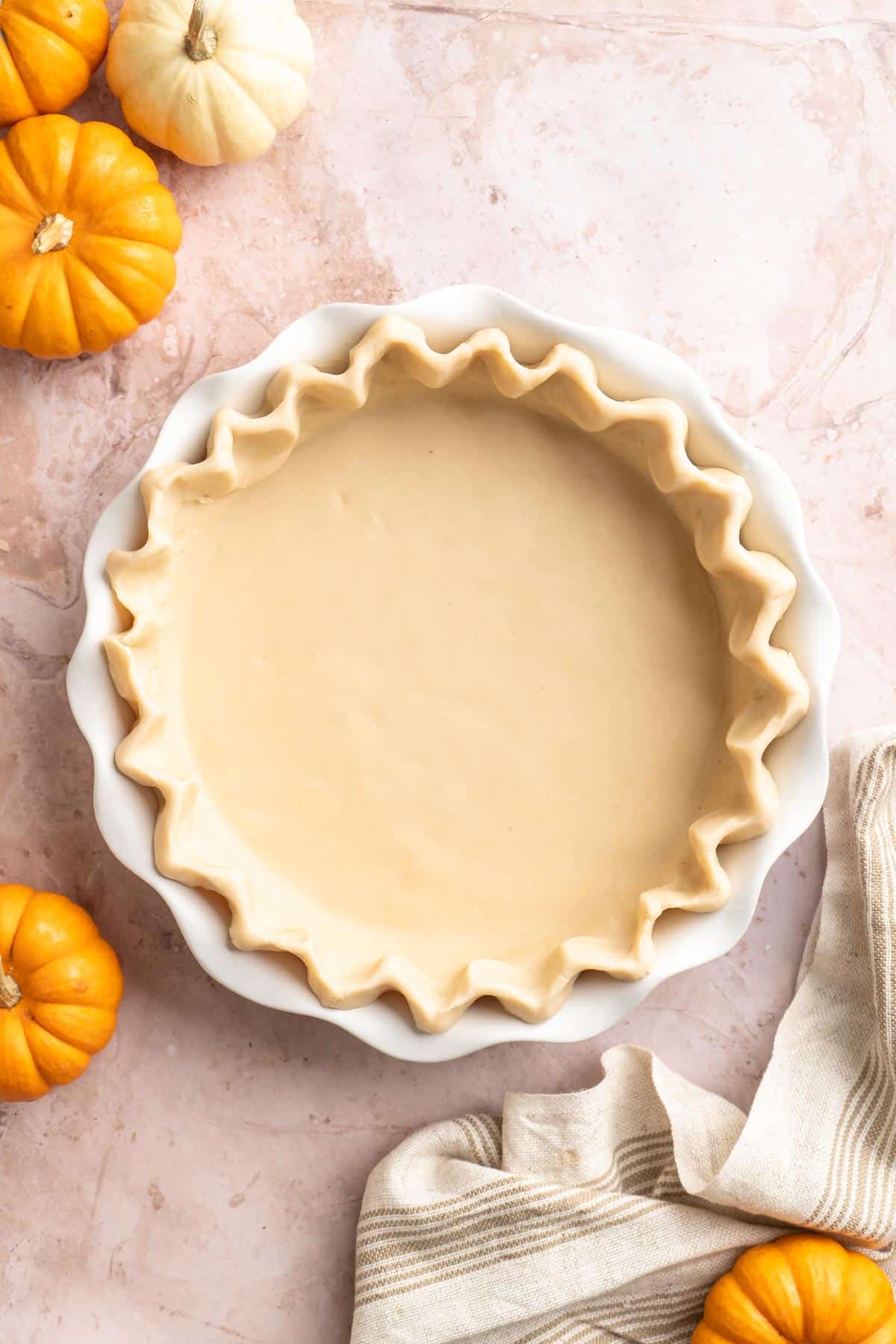 Pie crust in a pie plate near small pumpkins.