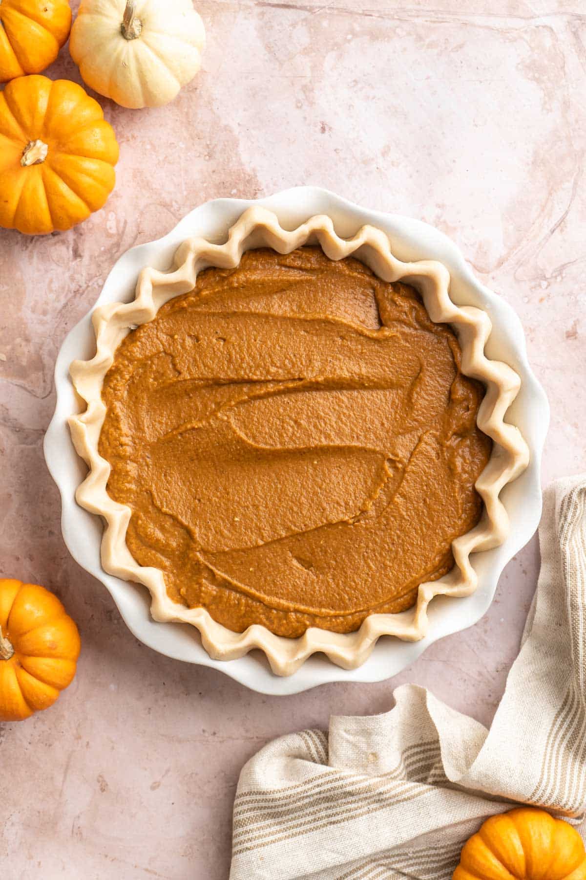 Pumpkin filling added to pie crust in a white pie plate.