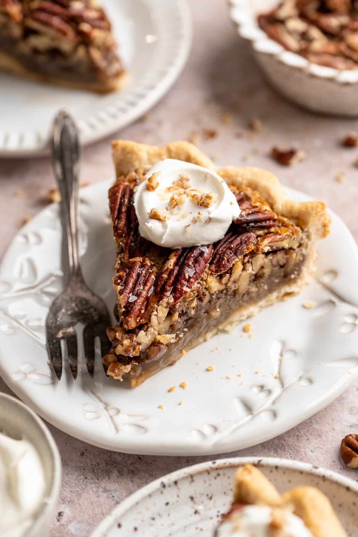 Slice of pecan pie on a white plate with a fork.