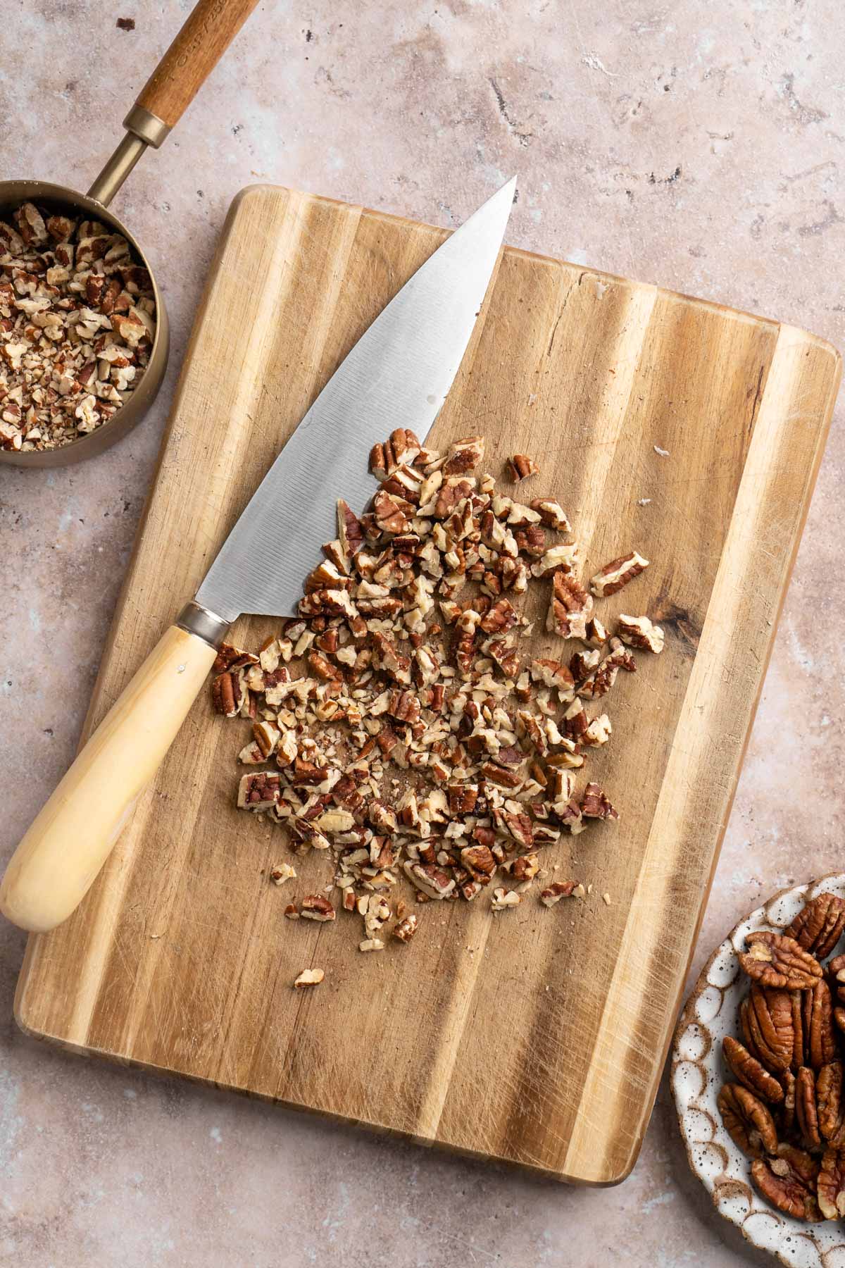 Chopped pecans on a cutting board near a sharp knife.