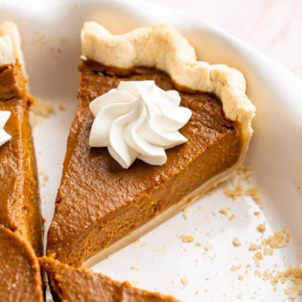 Slice of pumpkin pie in a pie plate topped with whipped cream.