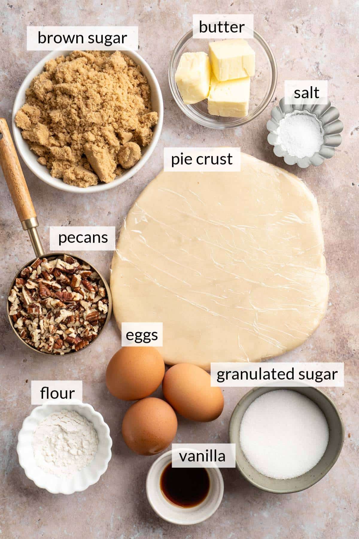 Pie crust near eggs, bowls of pecans, butter, sugar and vanilla.