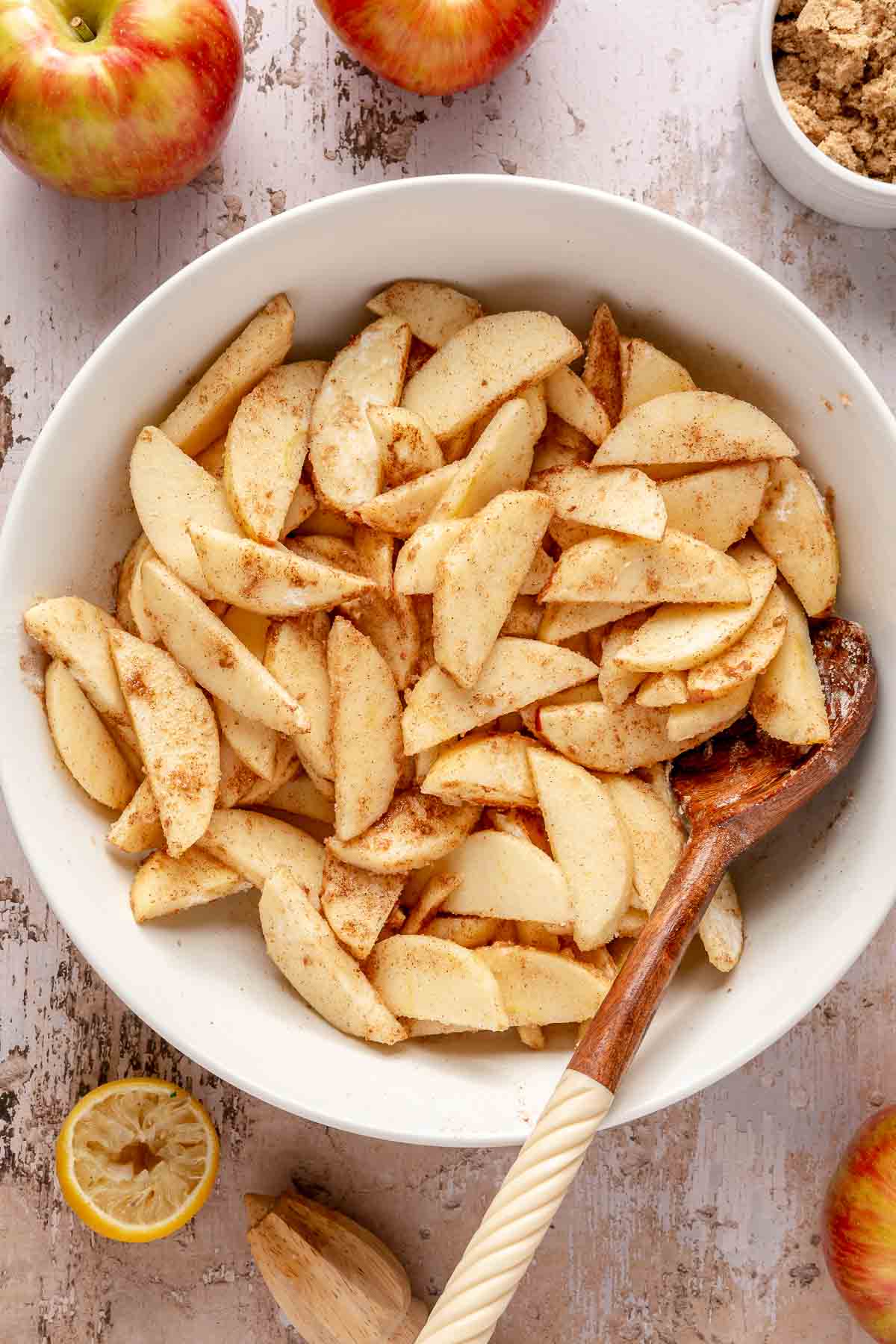 Tossing apple slices with cinnamon, sugar, flour and lemon juice in a white bowl.