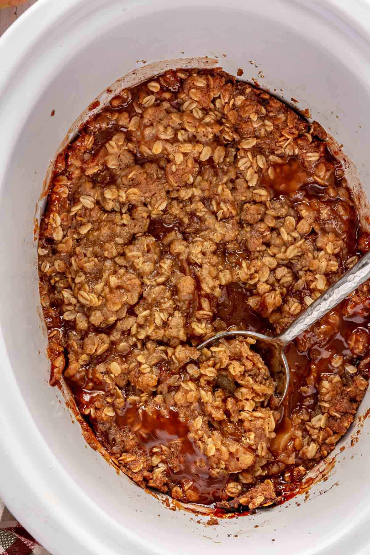 Using a serving spoon to scoop out slow cooker apple crisp.