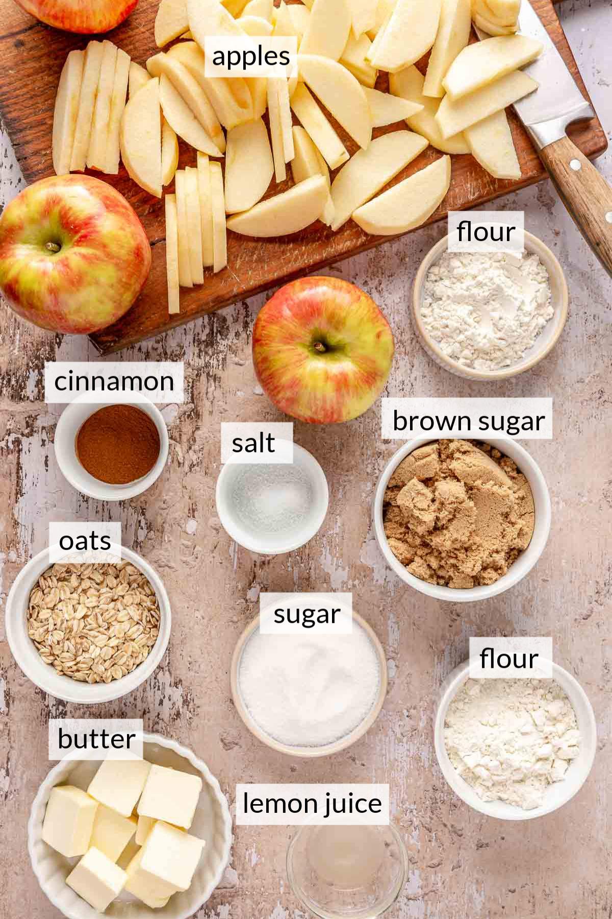 Sliced apples on a cutting board near bowls of flour, oats, sugar and cinnamon.