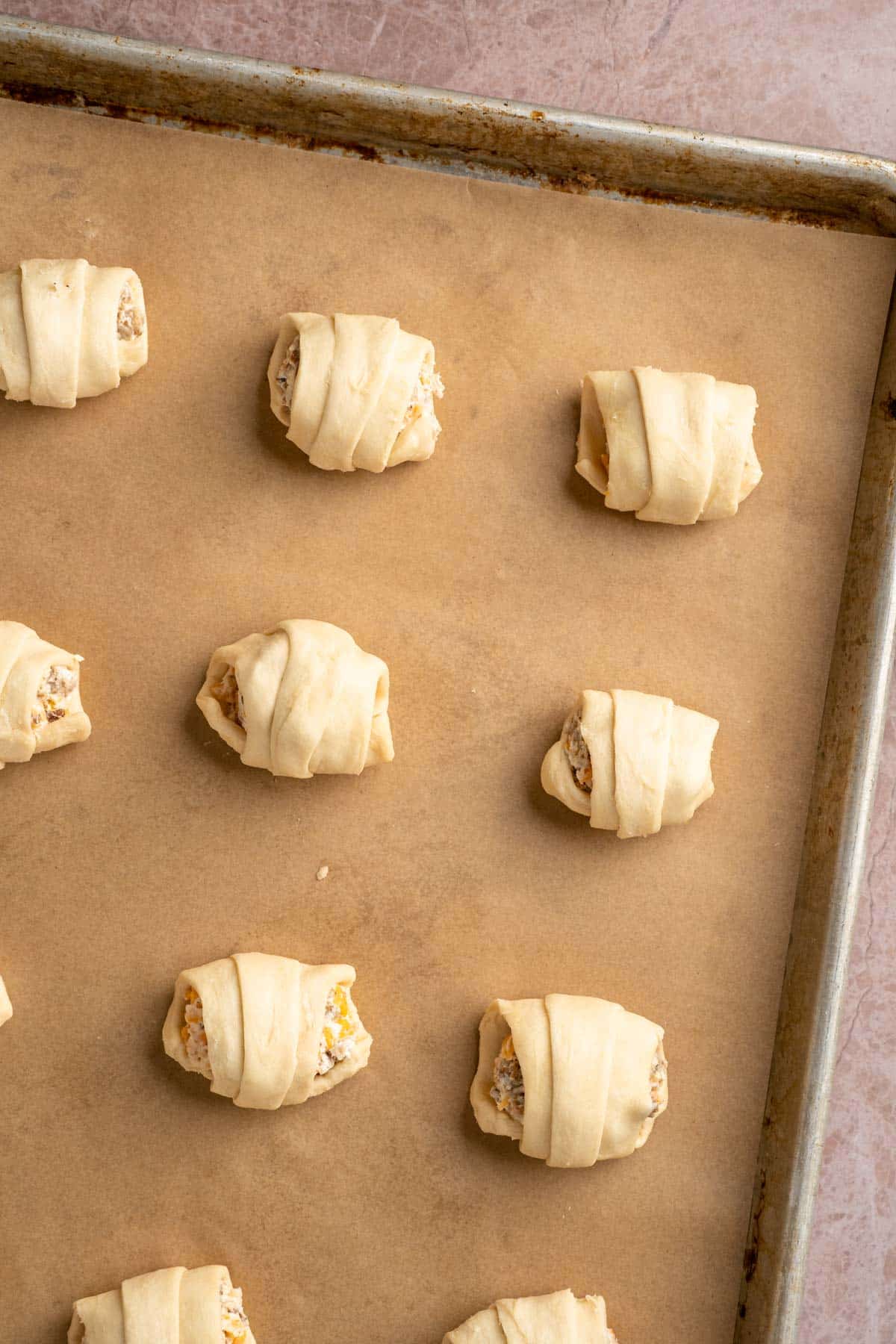 Crescent roll dough stuffed and rolled on a sheet pan.