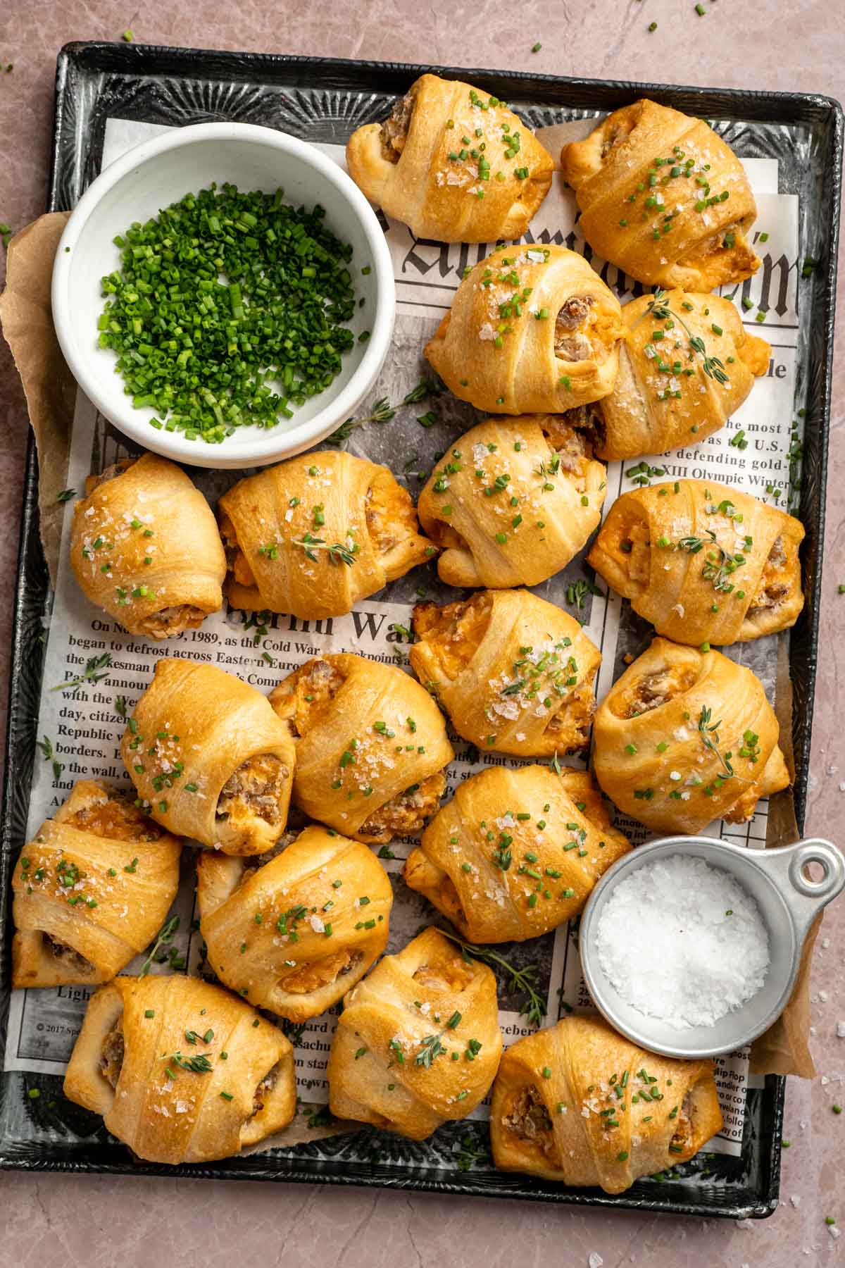 Breakfast crescent rolls on a baking pan with a bowl of chives and flaky salt.