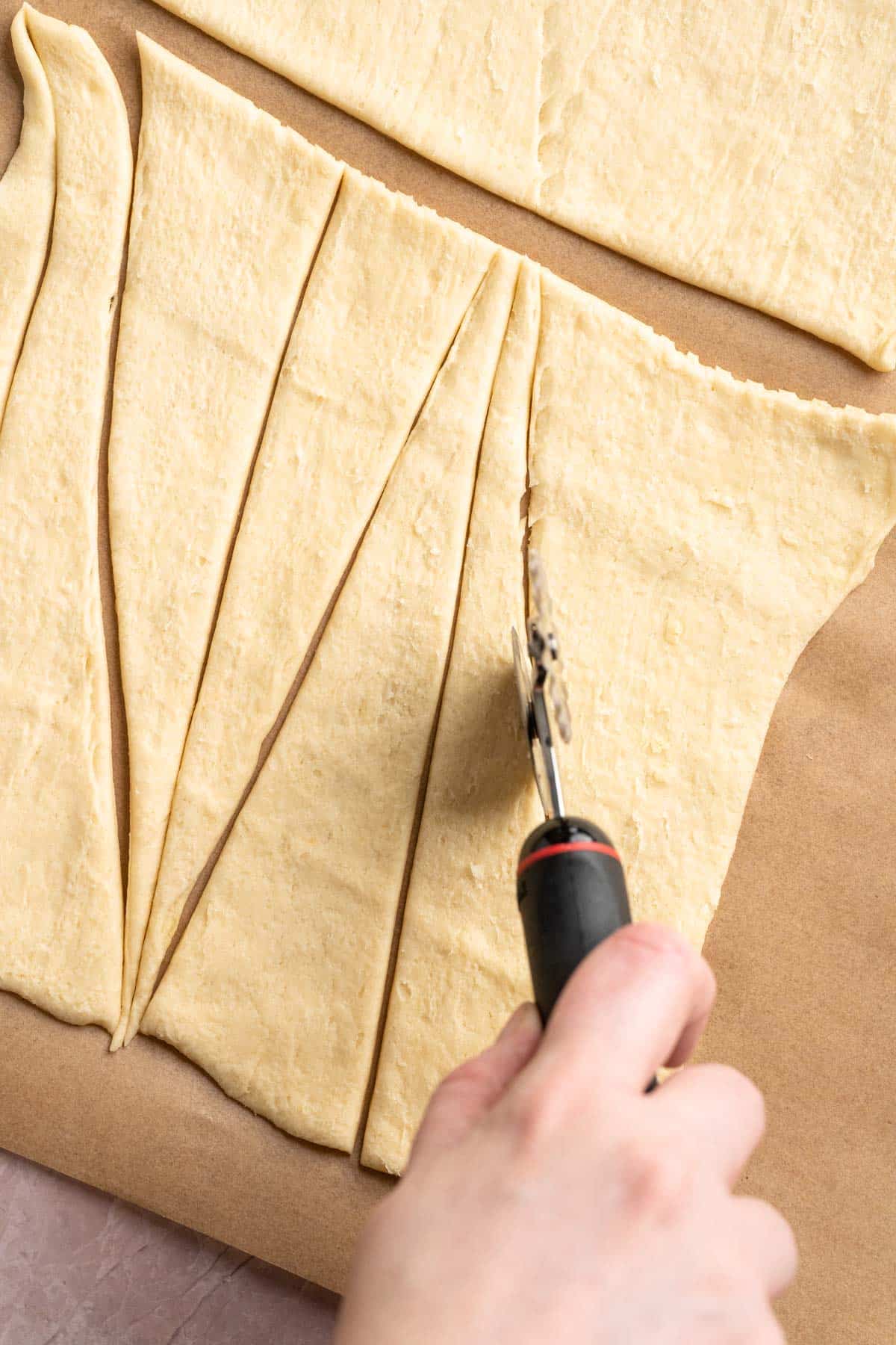 Using a pizza cutter to slice crescent roll dough.