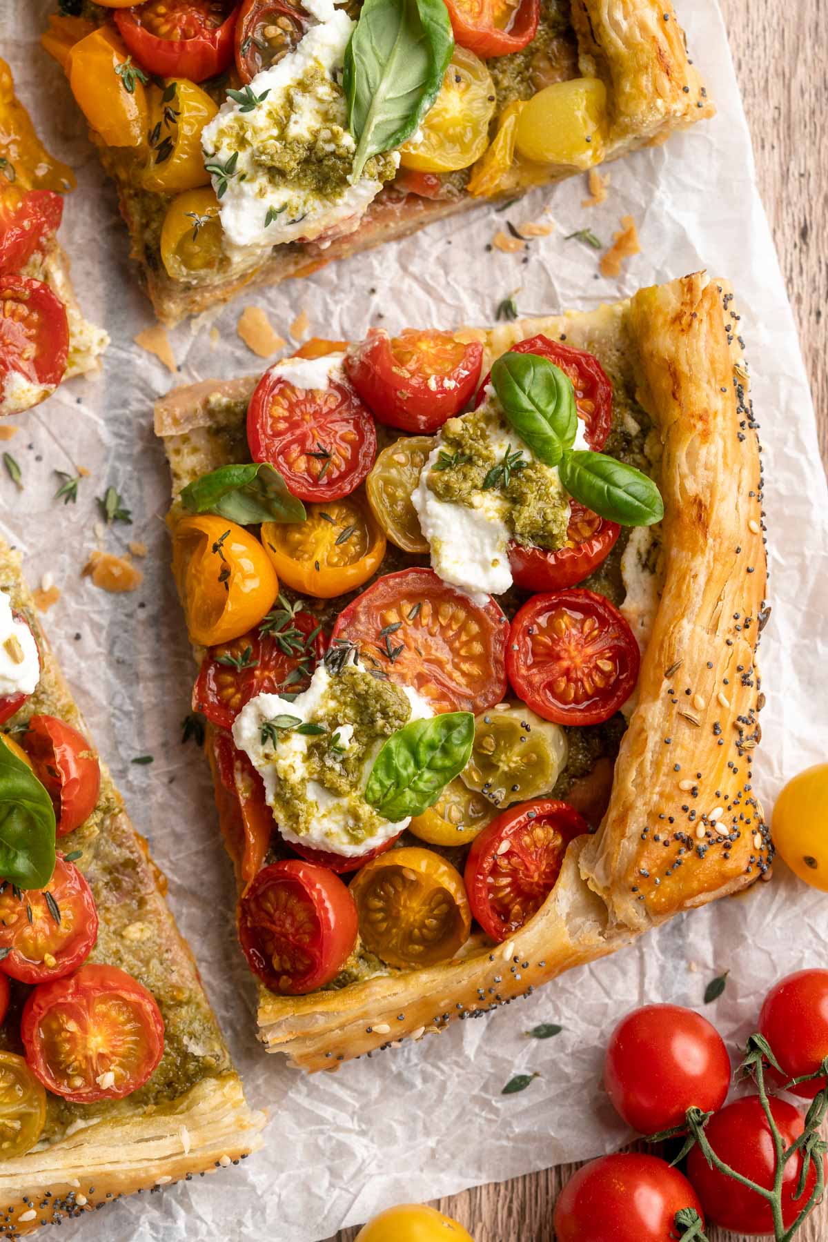 Sliced tomato tart on parchment paper with herbs.