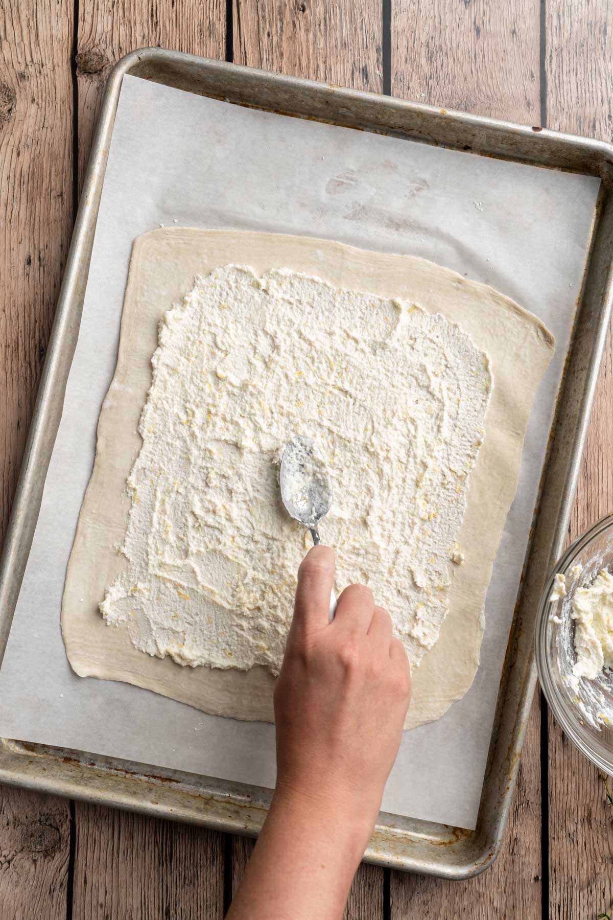 Spreading ricotta cheese over a puff pastry on a sheet pan.