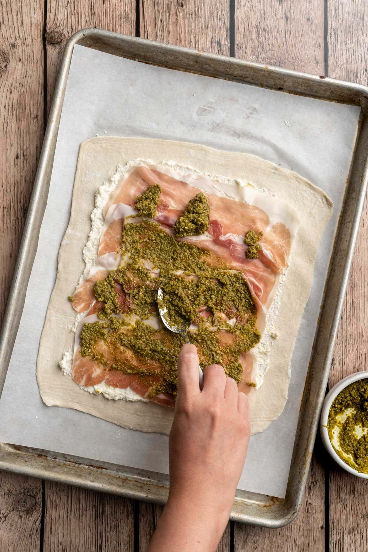 Spreading pesto over prosciutto on a puff pastry.