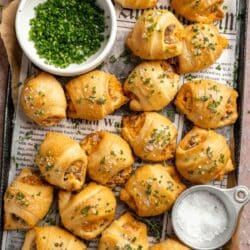 Breakfast crescent rolls on a baking pan with a bowl of chives and flaky salt.