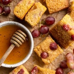 Grape cake squares near a bowl of honey and purple grapes.