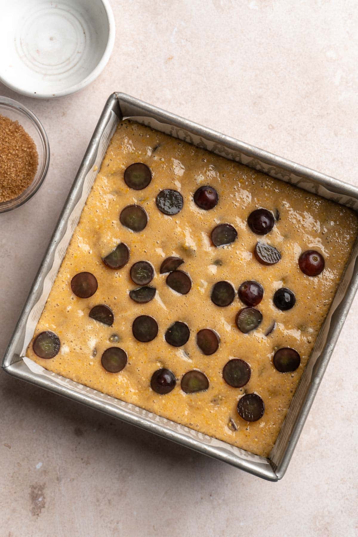 Adding grapes to the top of a partially baked cornmeal cake.