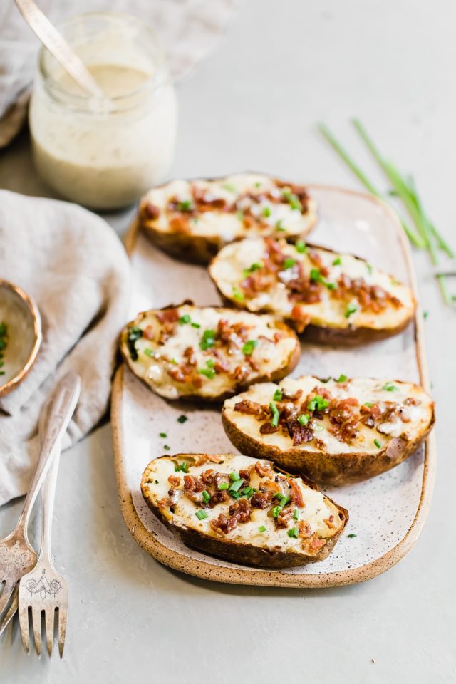 Potato skins on an oval serving platter, topped with bacon and chives