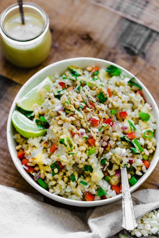 cauliflower rice salad in a large white serving bowl with lime slices on the side