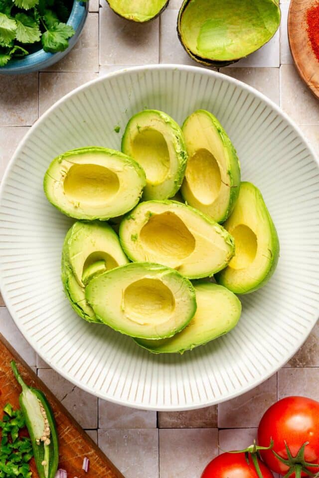 Peeled and seeded avocados in a white bowl.