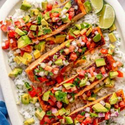 Pan seared salmon with avocado salsa served over rice on a large white plate.