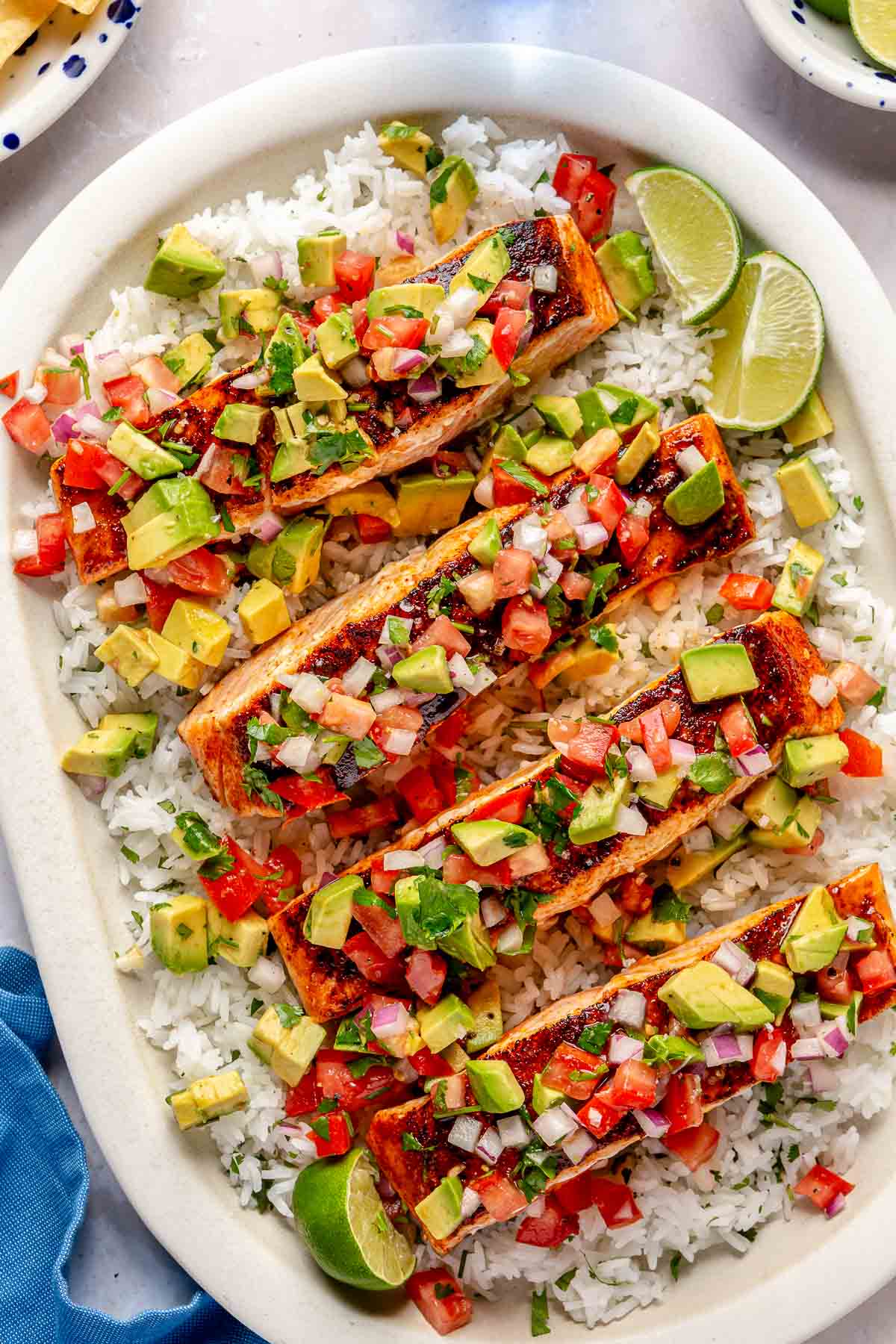 Pan seared salmon with avocado salsa served over rice on a large white plate.