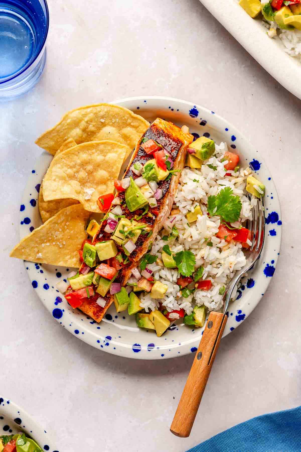 Pan seared salmon on a plate with rice, tortilla chips and avocado salsa.