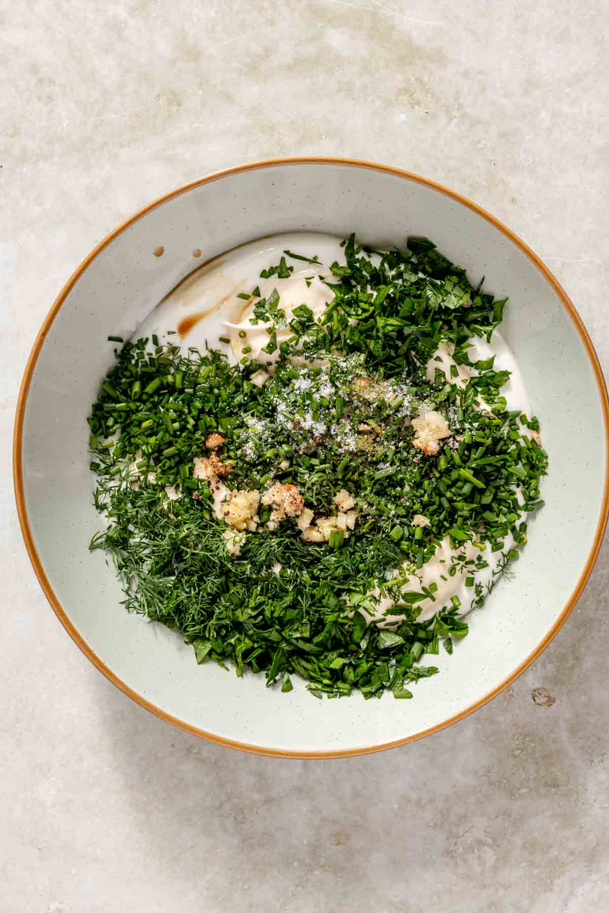 Greek yogurt and mayo added to a bowl with fresh dill and parsley.