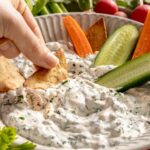 Hand dipping a cracker in ranch dip.