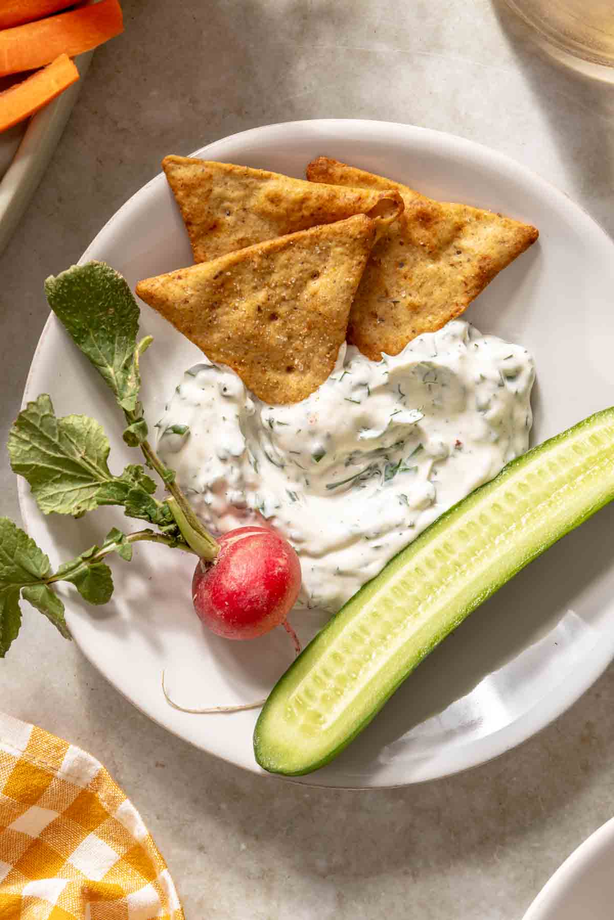 Ranch dip served on a small white plate with a radish, cucumber and crackers.