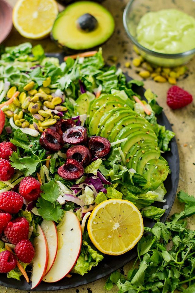 large salad topped with sliced avocado, raspberries, cherries and sliced apple