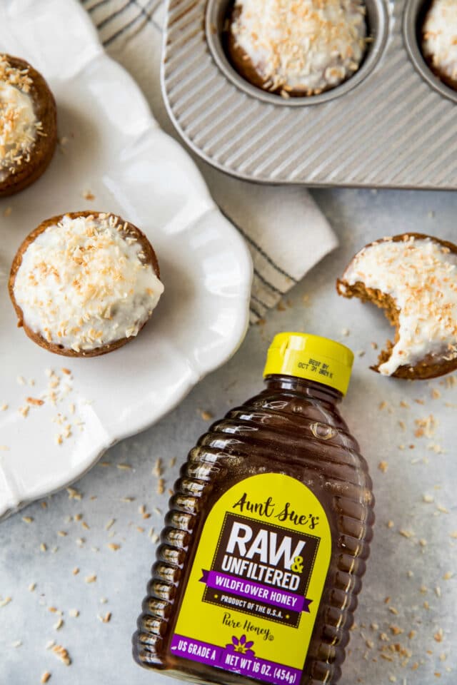 bottle of honey near muffins that have a white icing