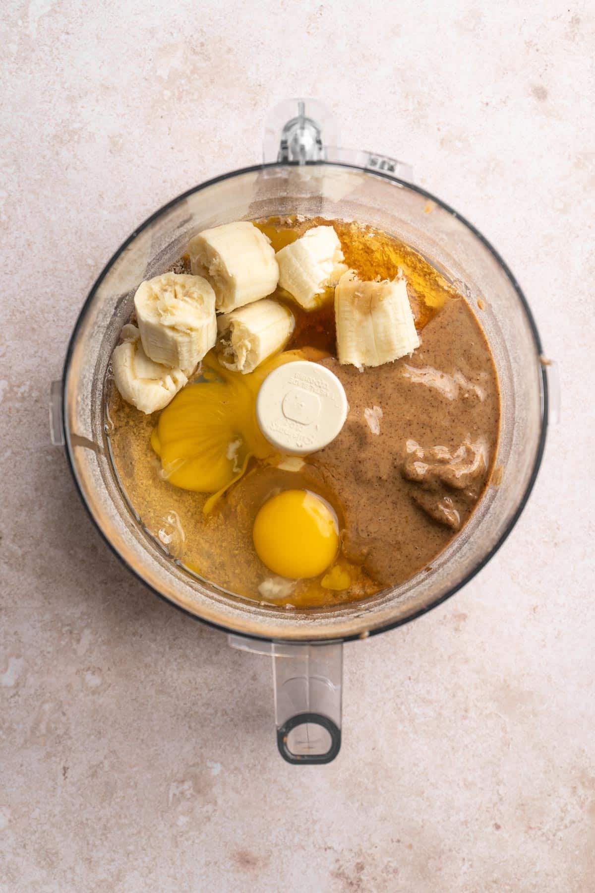 Adding almond butter, eggs and banana chunks to a food processor.