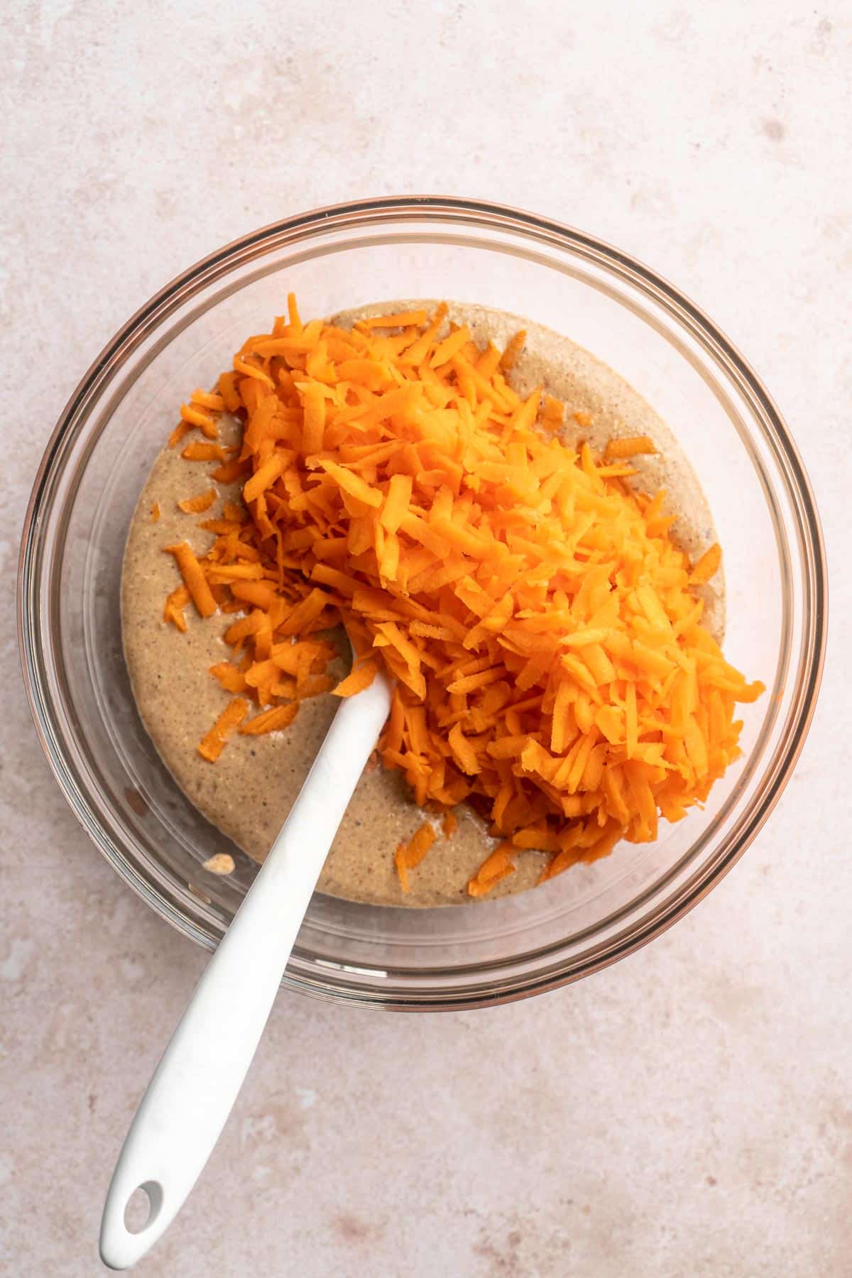 Stirring shredded carrots into muffin batter in a bowl.