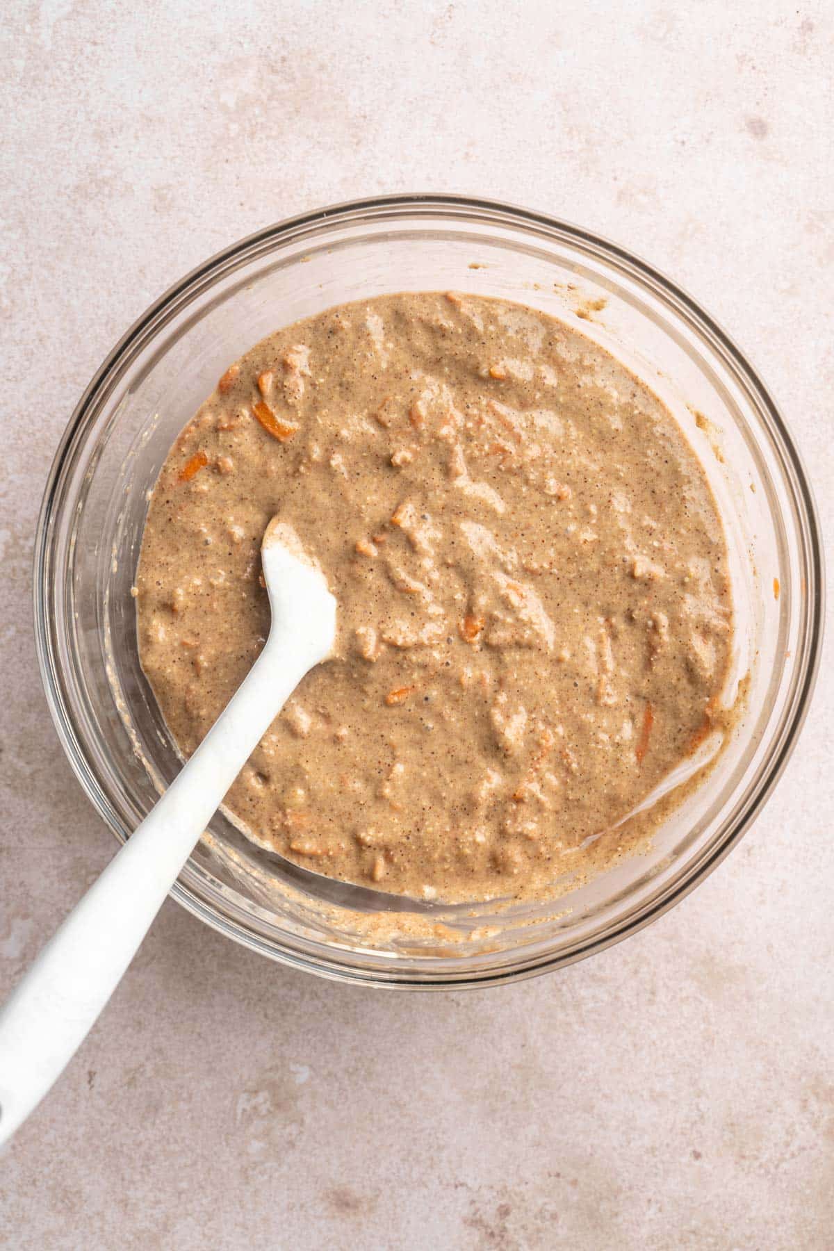 Stirring muffin batter with a white spatula in a glass bowl.