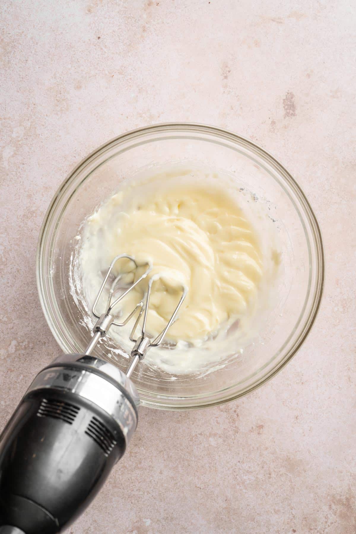 Beating cream cheese with powdered sugar and milk in a bowl.