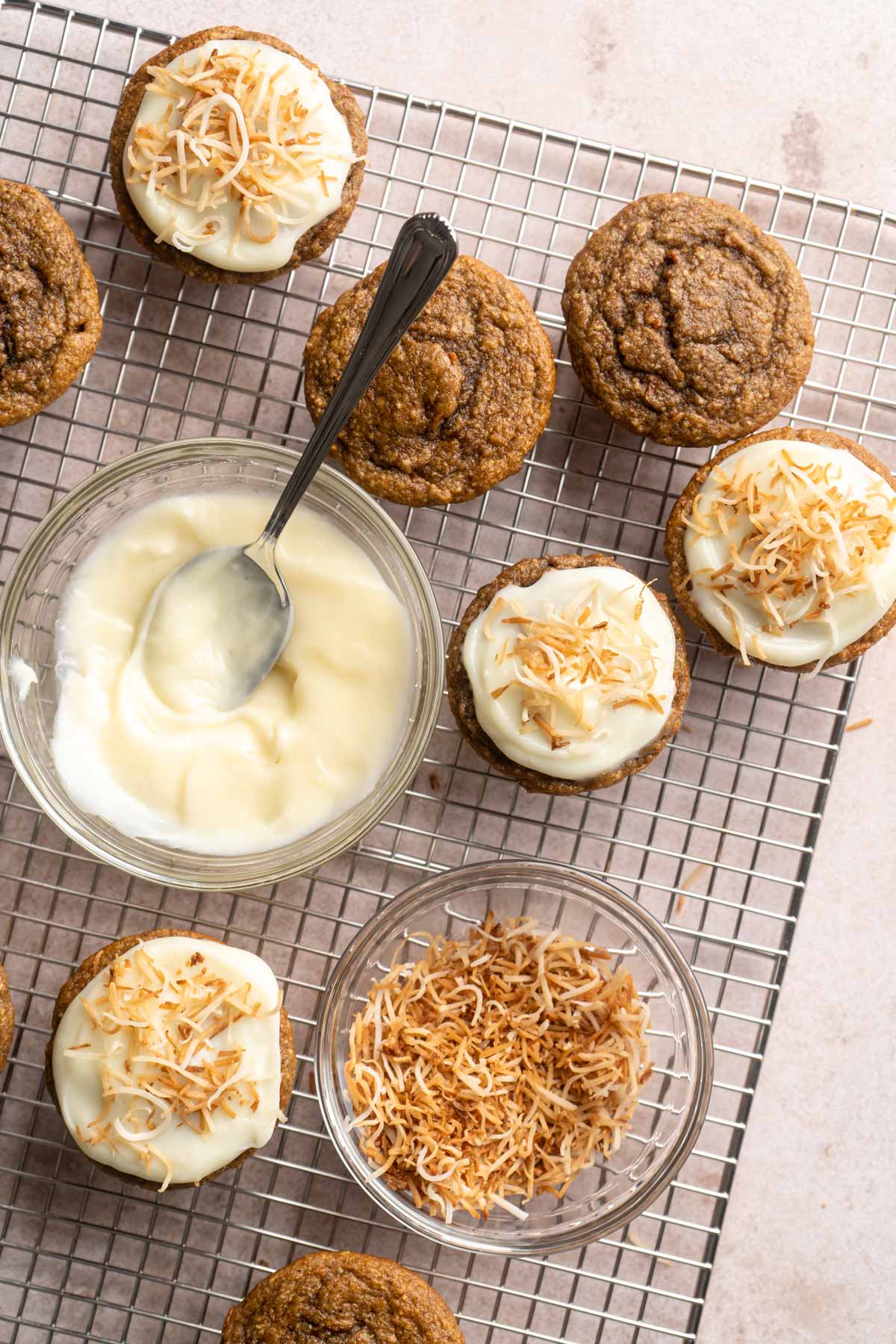 Topping muffins with icing and toasted shredded coconut on a wire rack.