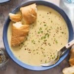 Potato leek soup served in a blue bowl with crusty bread.