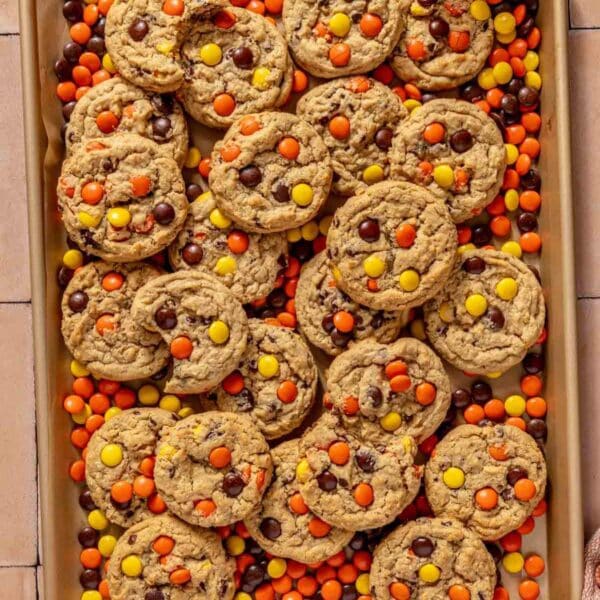 Peanut butter Reese's cookies on a baking sheet with Reese's pieces.