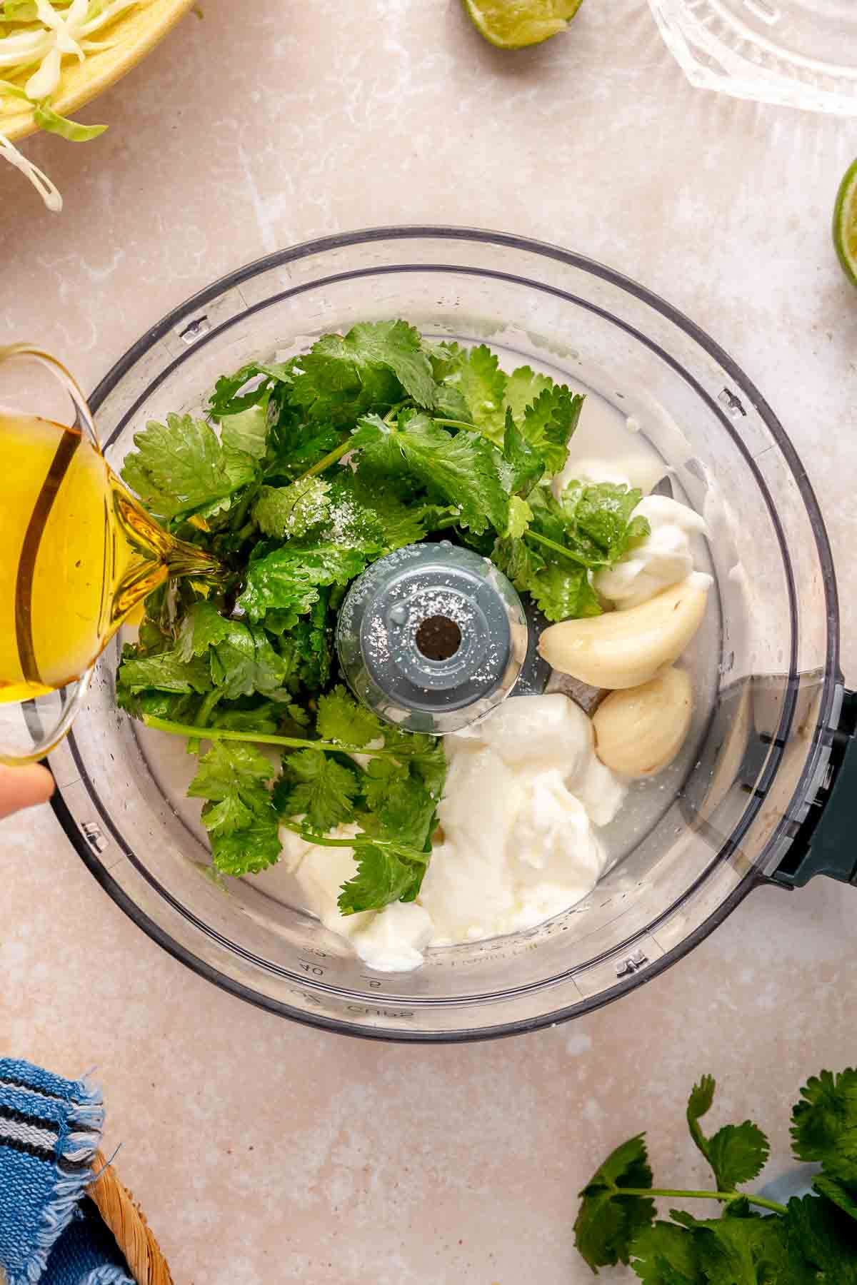 Pouring oil into a food processor with cilantro, sour cream and garlic.