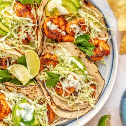 Shrimp tacos with cilantro lime slaw on a plate with lime wedges and avocado slices.