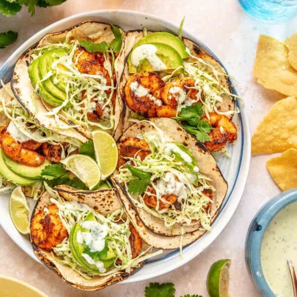 Shrimp tacos with cilantro lime slaw on a plate with lime wedges and avocado slices.