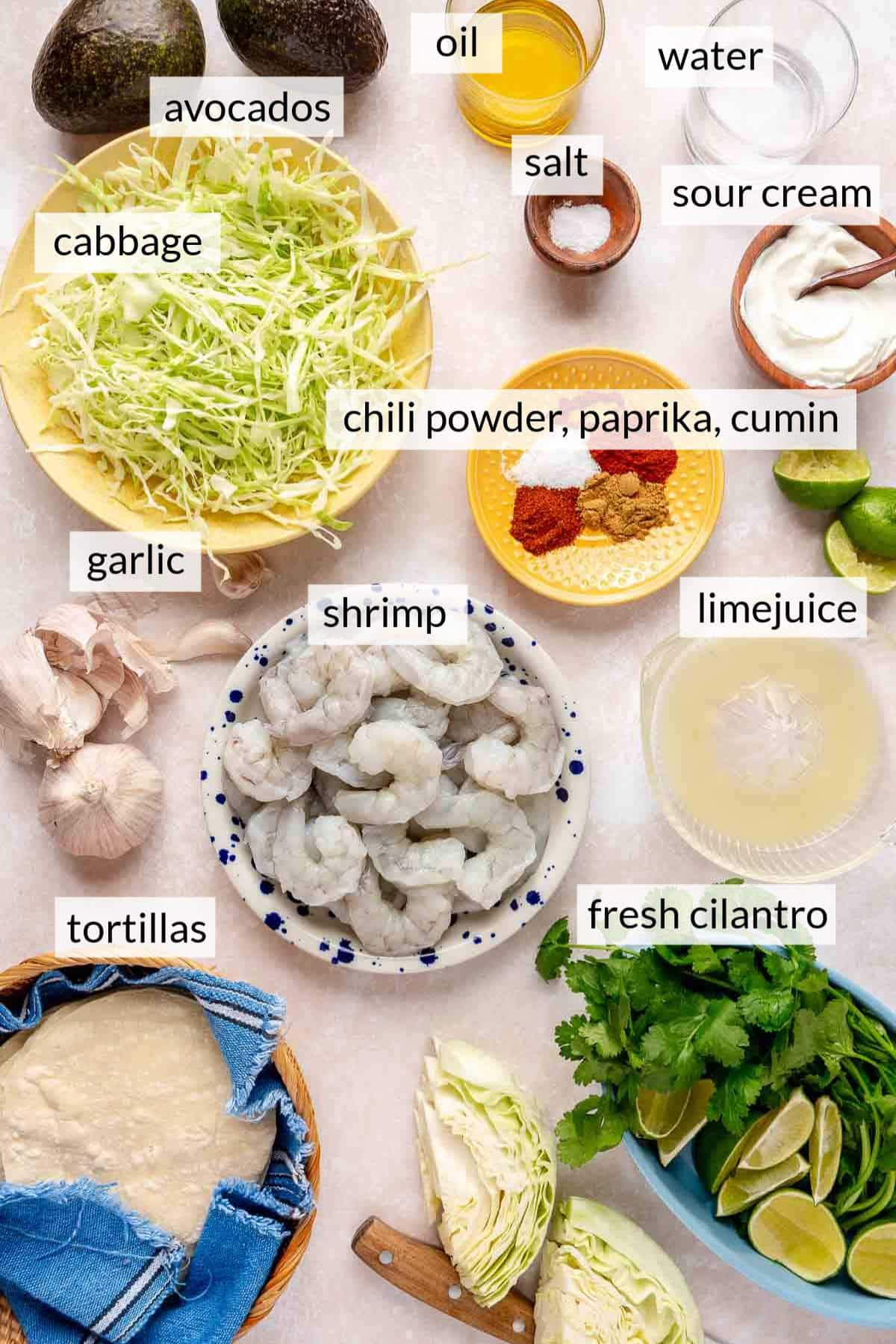 Shrimp in a bowl near cabbage, avocados, limes, tortillas and fresh cilantro.