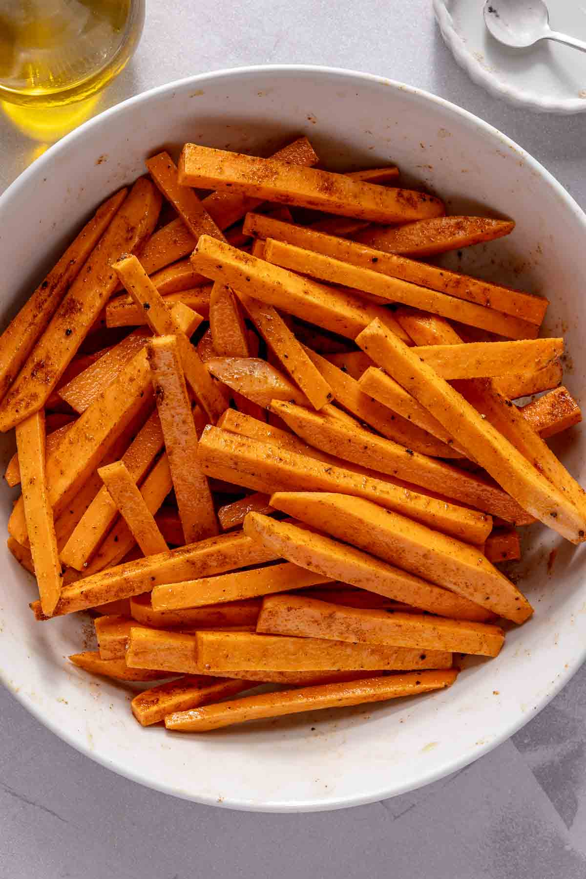 Uncooked sweet potato slices tossed with olive oil and spices in a bowl.