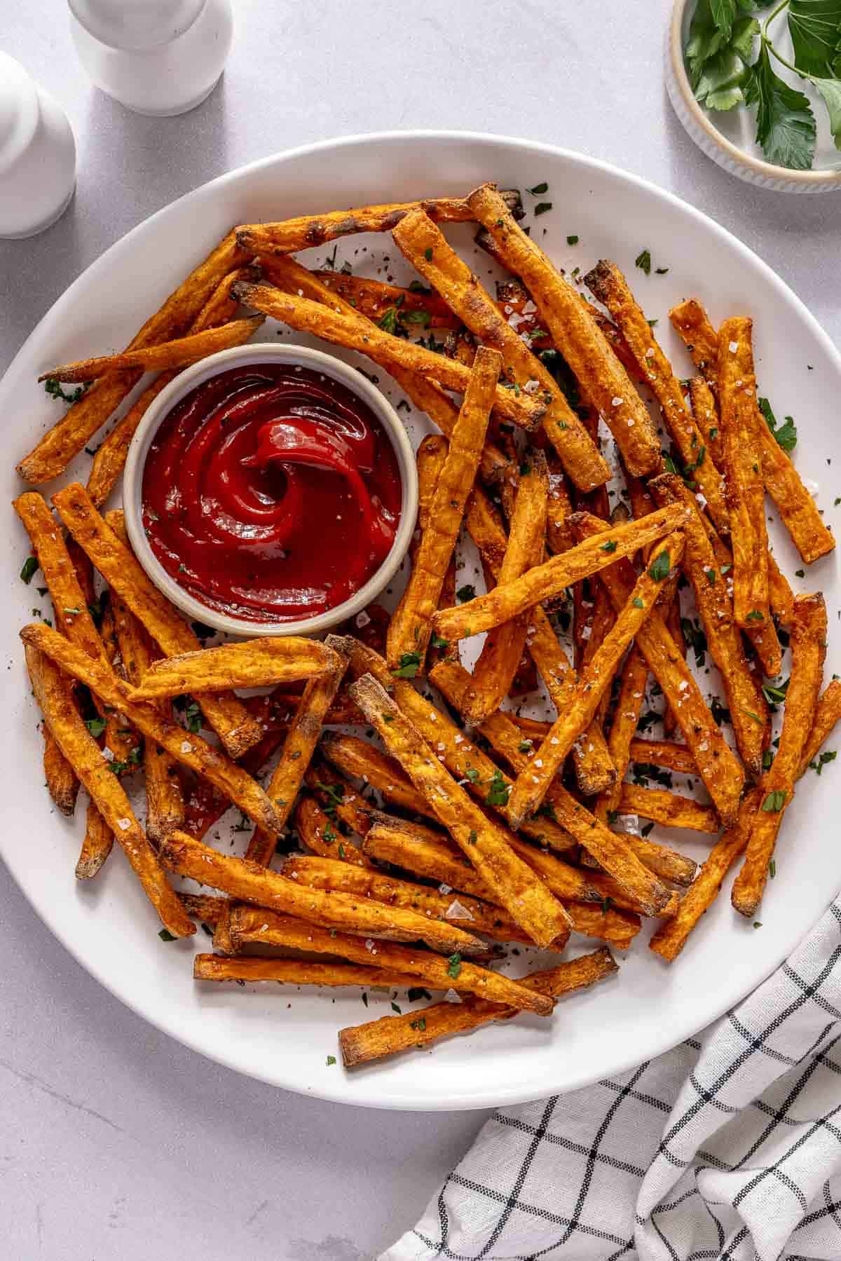 Baked sweet potato fries served on a white plate with a small bowl of ketchup.