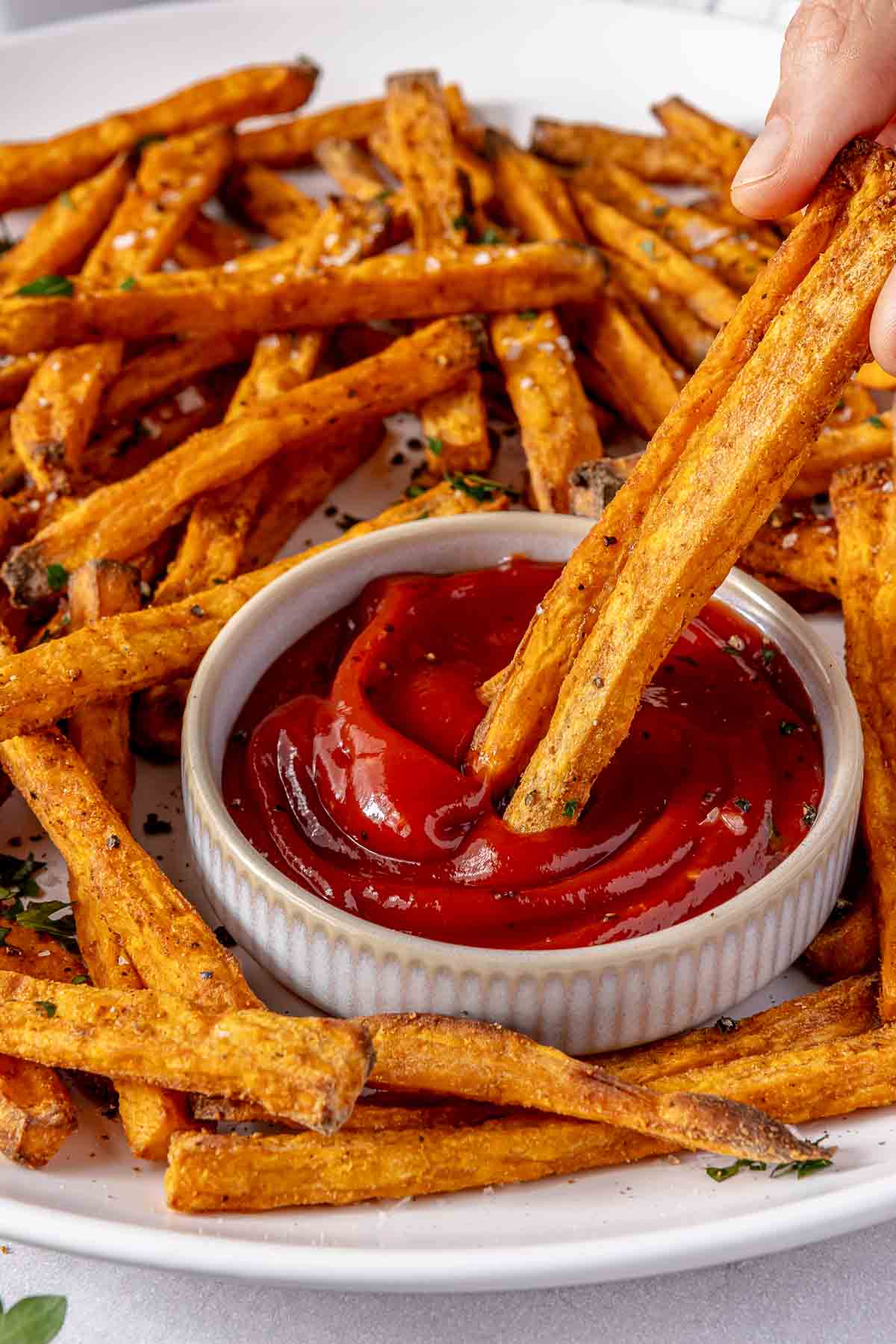 Hand dipping sweet potato fries into a small bowl of ketchup.