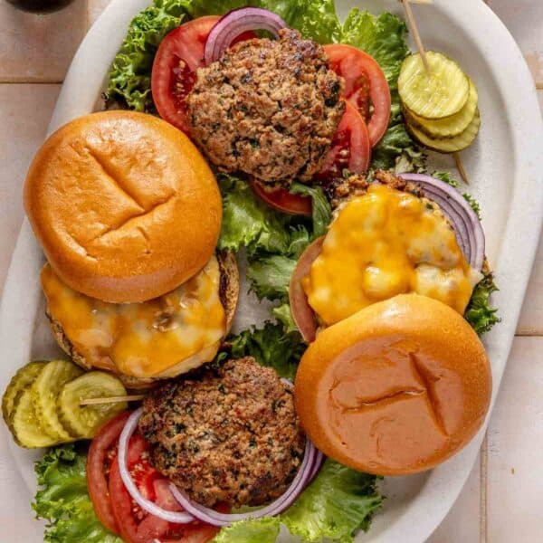 Turkey burgers on a serving plate with sliced tomatoes, pickles and lettuce.