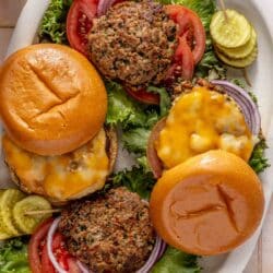 Turkey burgers on a serving plate with sliced tomatoes, pickles and lettuce.