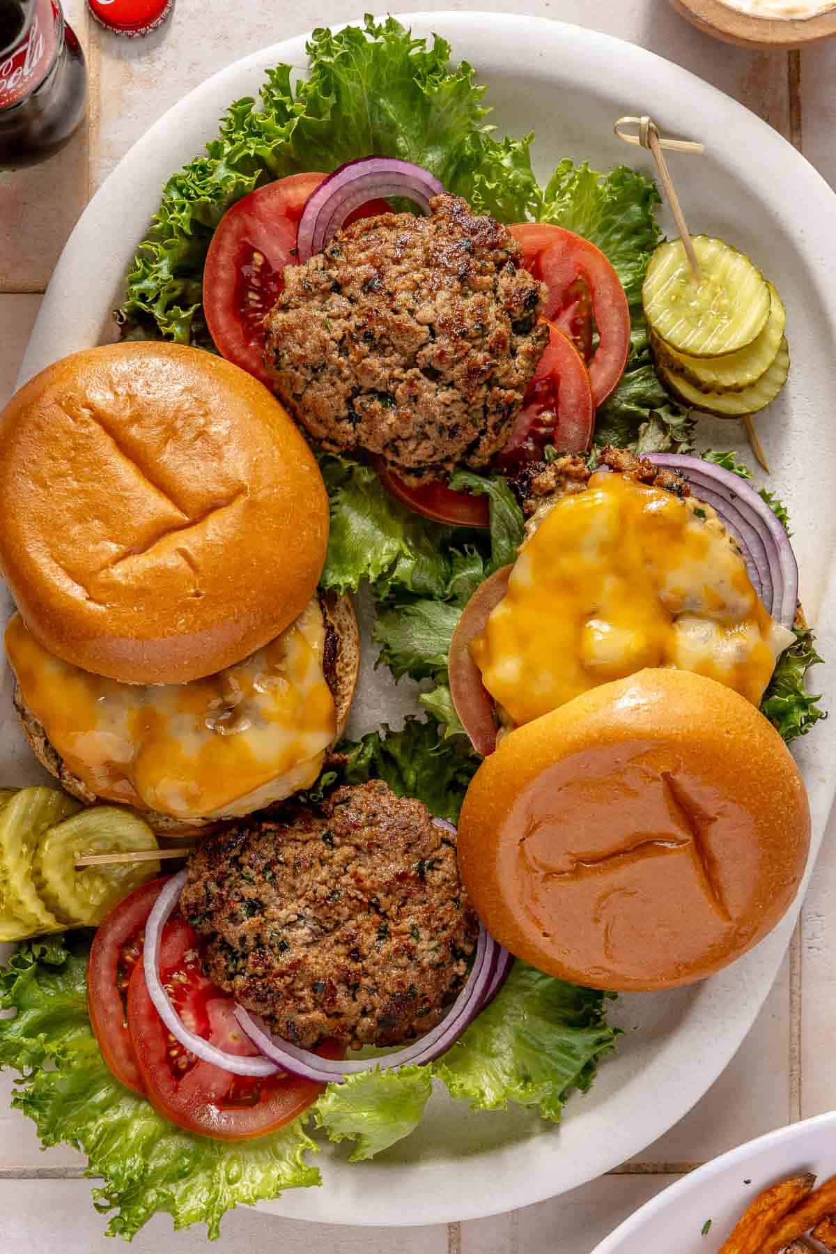 Turkey burgers on a serving plate with sliced tomatoes, pickles and lettuce.