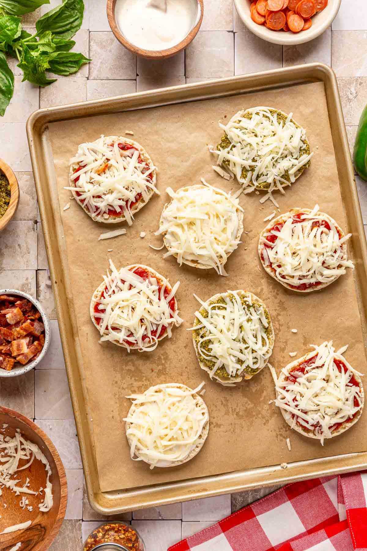 Shredded cheese on top of mini pizzas on a pan.