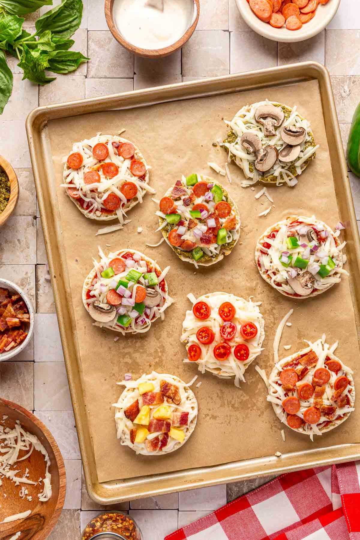 English muffin pizzas on a baking pan before being cooked.