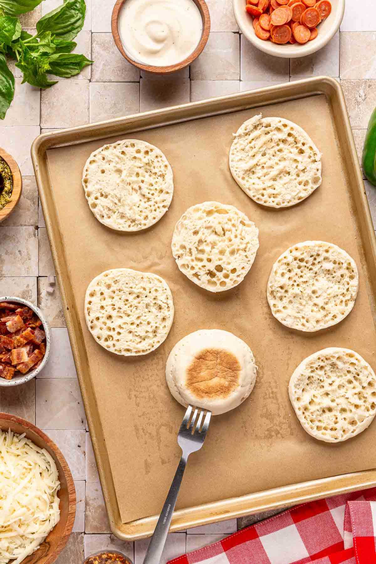 Halves of English muffins on a parchment-lined baking sheet.